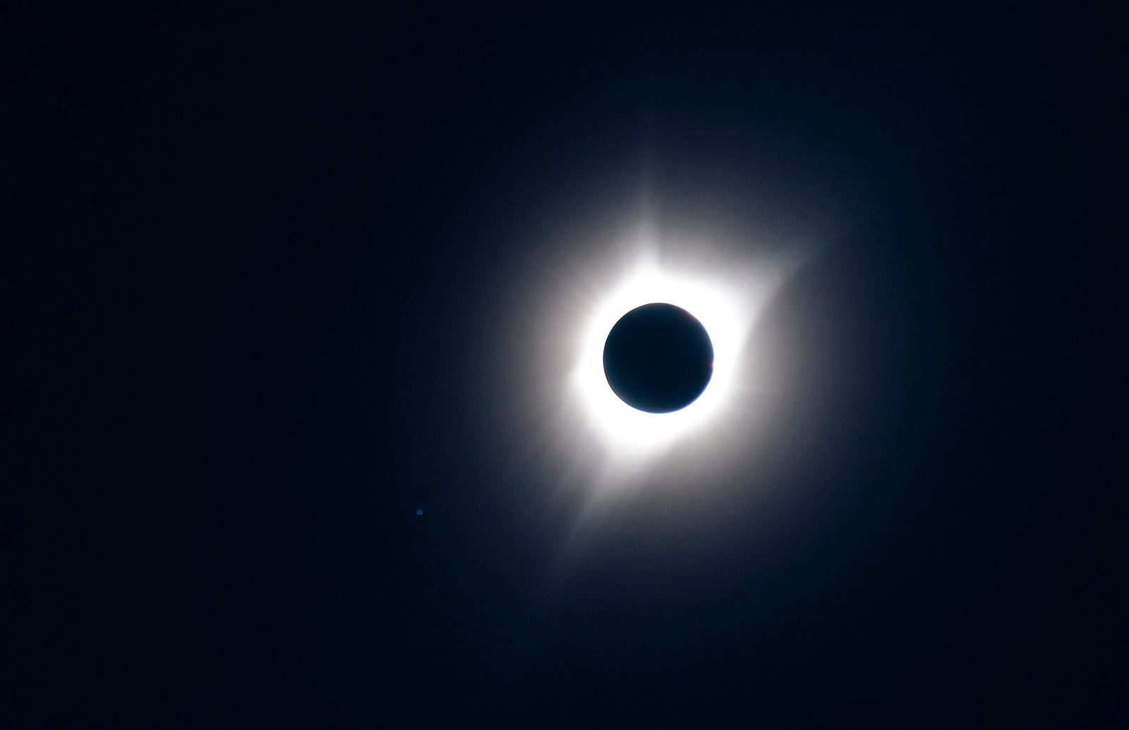 Un'eclissi solare totale in un cielo blu scuro, con la corona luminosa attorno al disco nero della Luna
