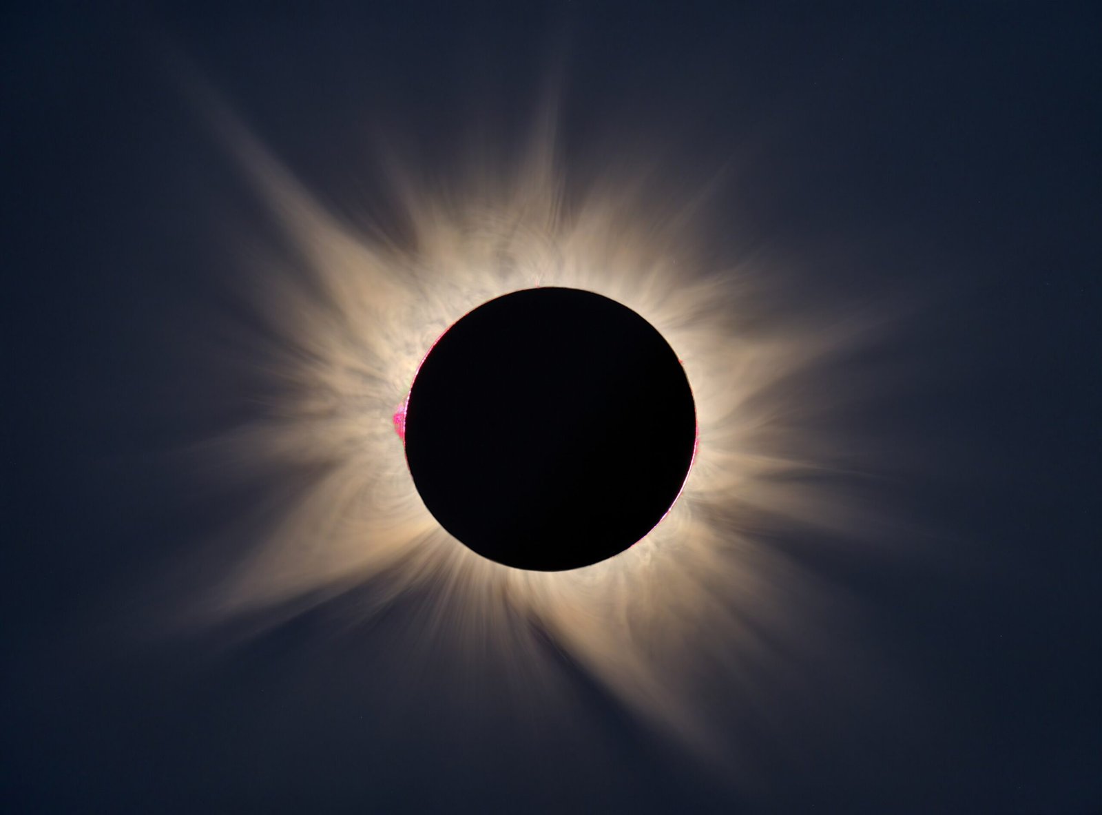 Un'eclissi solare totale con la corona del Sole in raggi dorati attorno alla Luna nera, in un cielo blu scuro