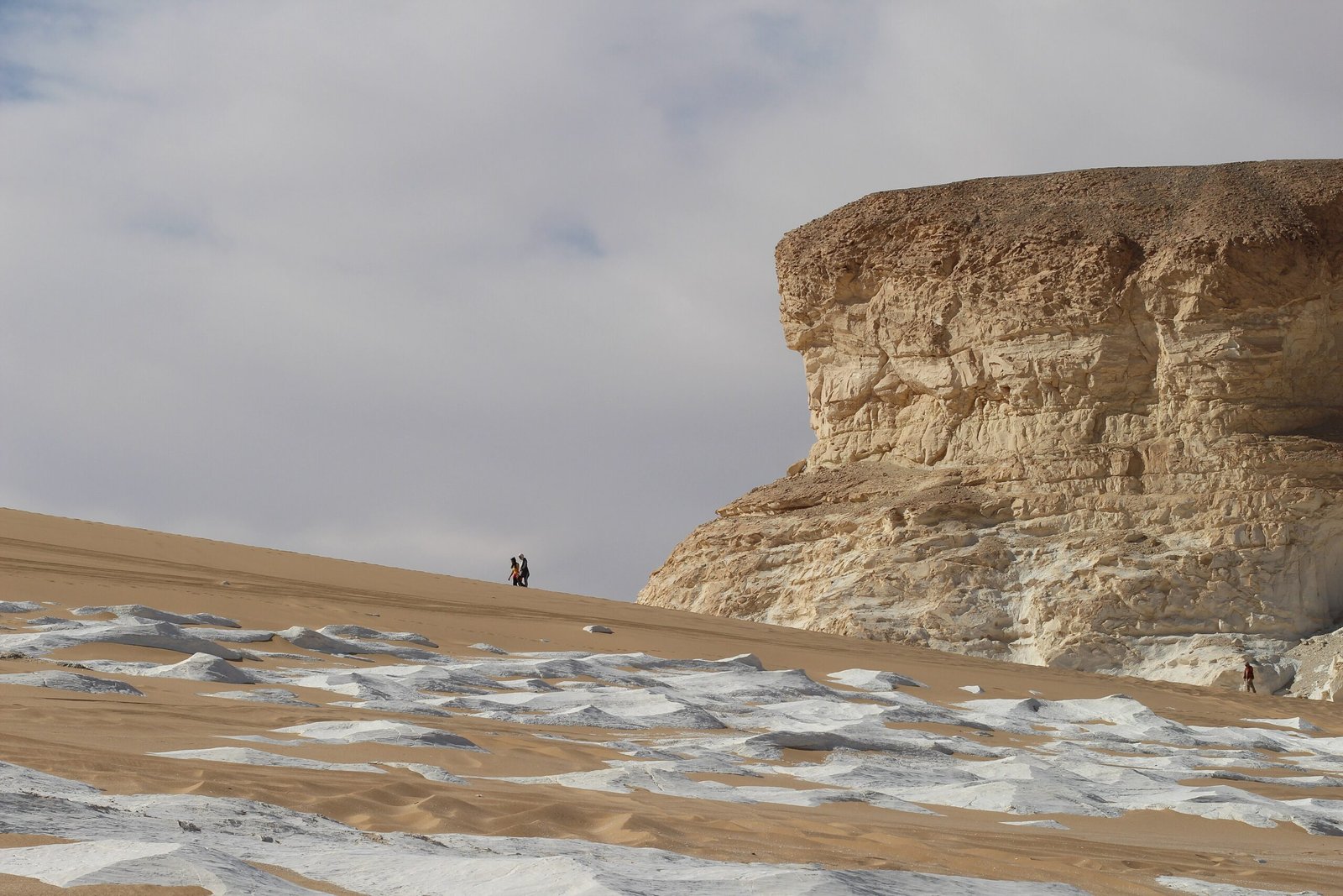 Una parete di gesso e calcare bianco nel Deserto Bianco, con due escursionisti lontani sulla duna