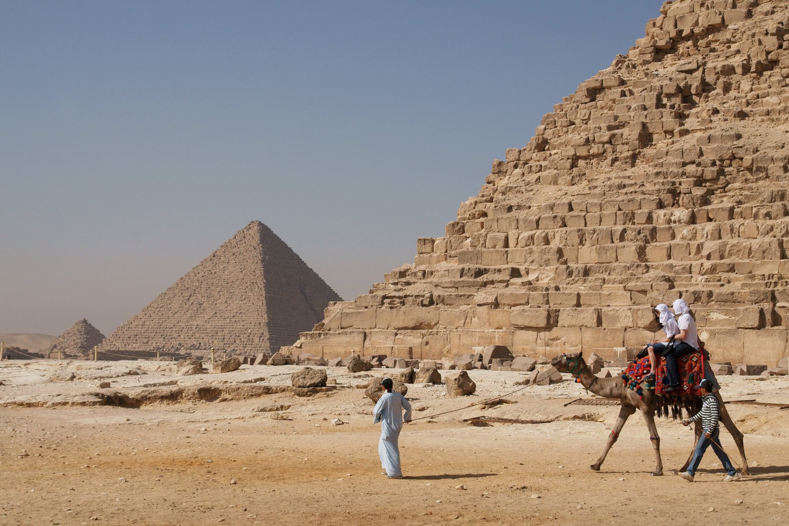 Un cammello con un visitatore davanti ai blocchi di una piramide di Giza e alla piramide minore sullo sfondo