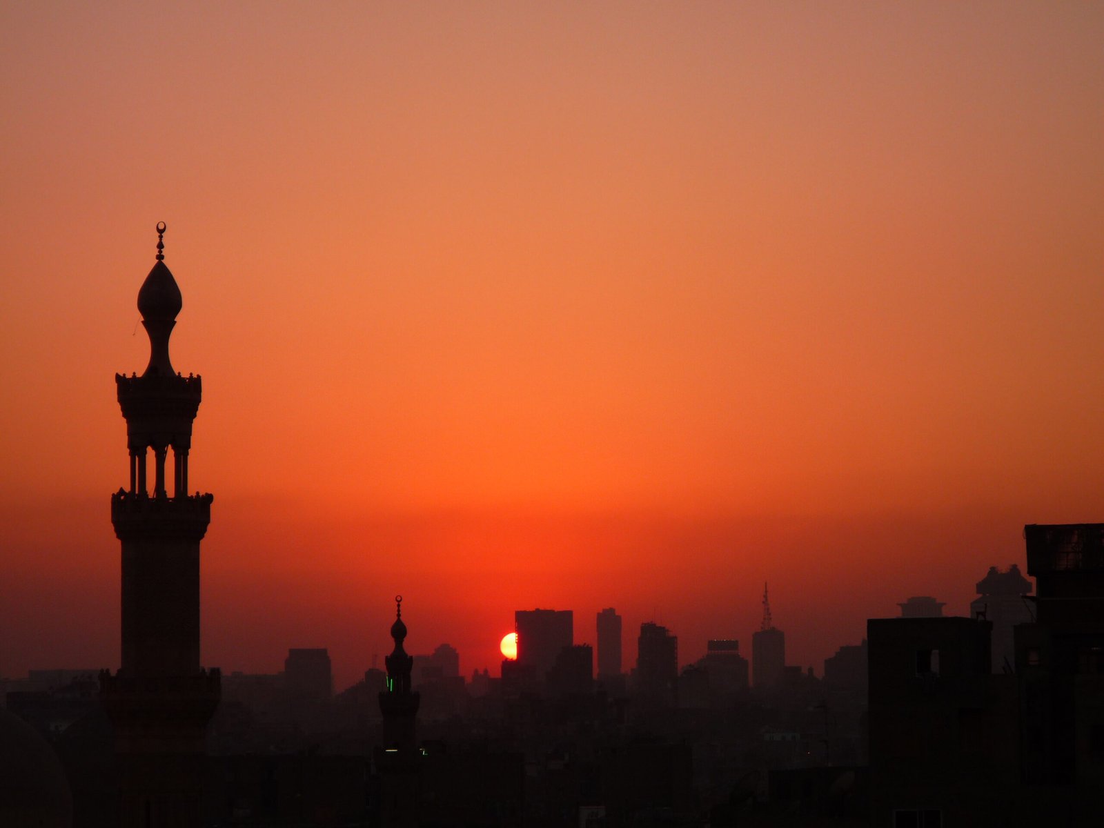 Il sole rosso all'orizzonte dietro i minareti del Cairo, con la sagoma di un minareto in controluce