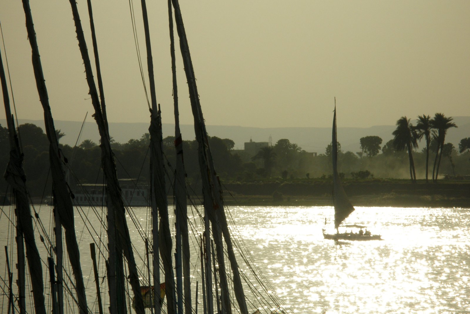 Gli alberi delle feluche in primo piano e una barca a vela nel riflesso del sole sul Nilo a Luxor