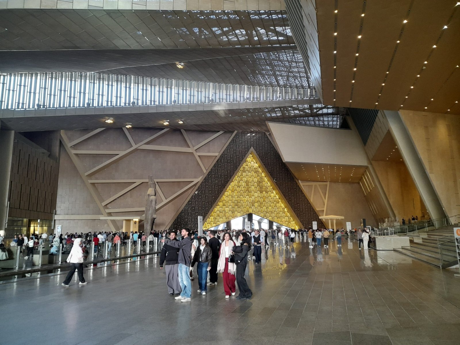 L'atrio del Grand Egyptian Museum con l'ingresso triangolare illuminato in fondo e i visitatori
