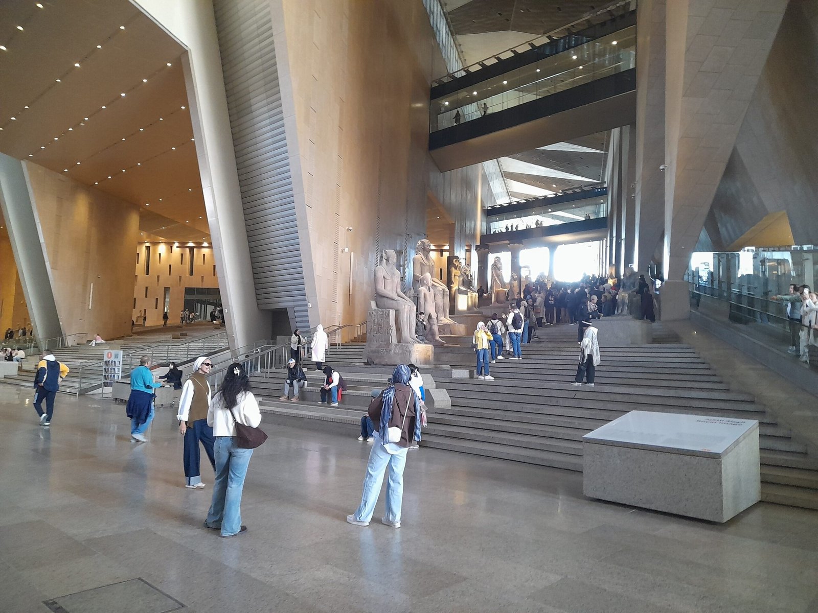 La grande scalinata del Grand Egyptian Museum con le statue colossali in cima e i visitatori in salita