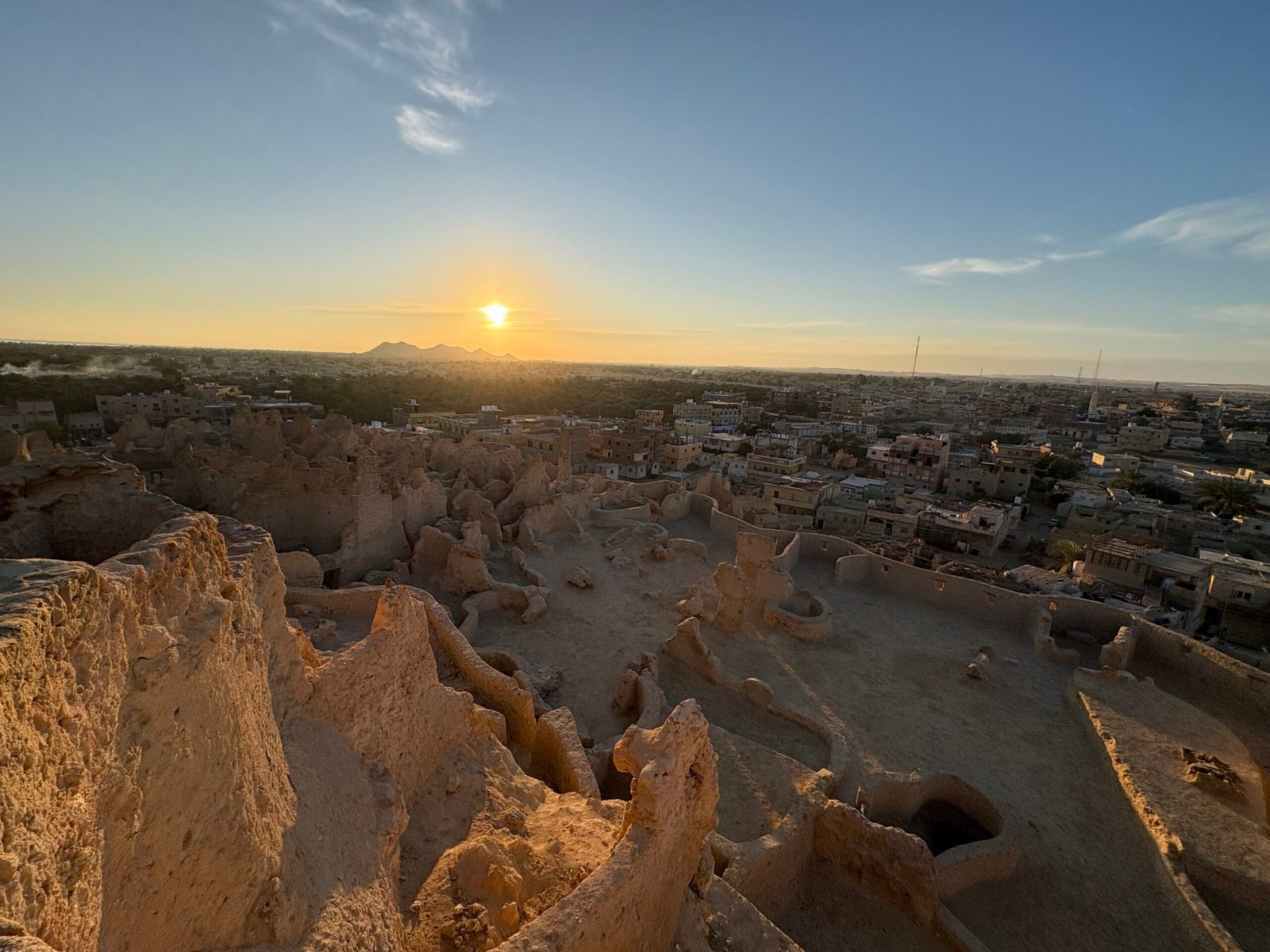 Il sole che tramonta sulle rovine di argilla e sale di Shali a Siwa, con l'oasi e la città sullo sfondo