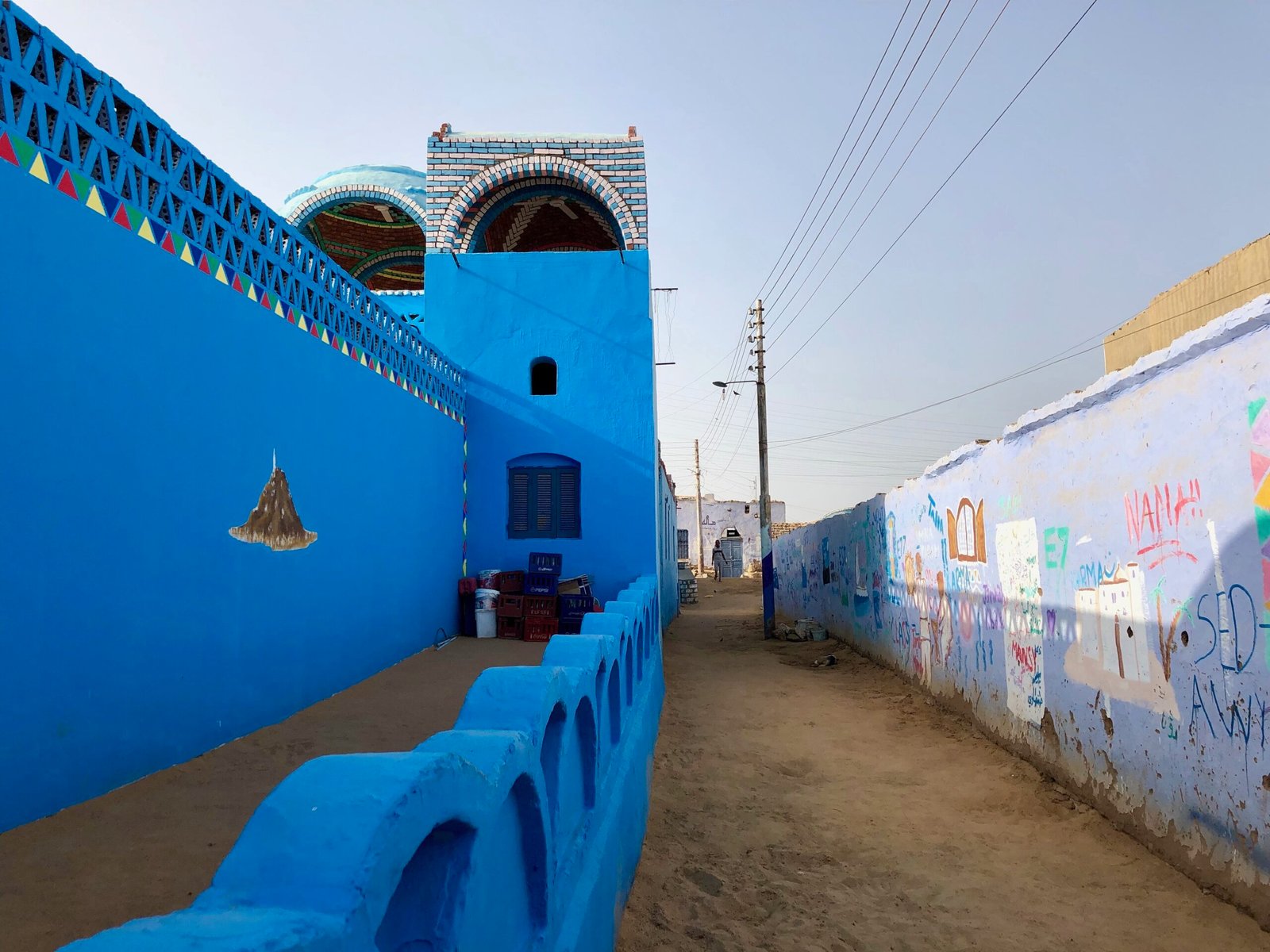 Un vicolo di sabbia tra muri blu decorati in un villaggio nubiano vicino ad Assuan