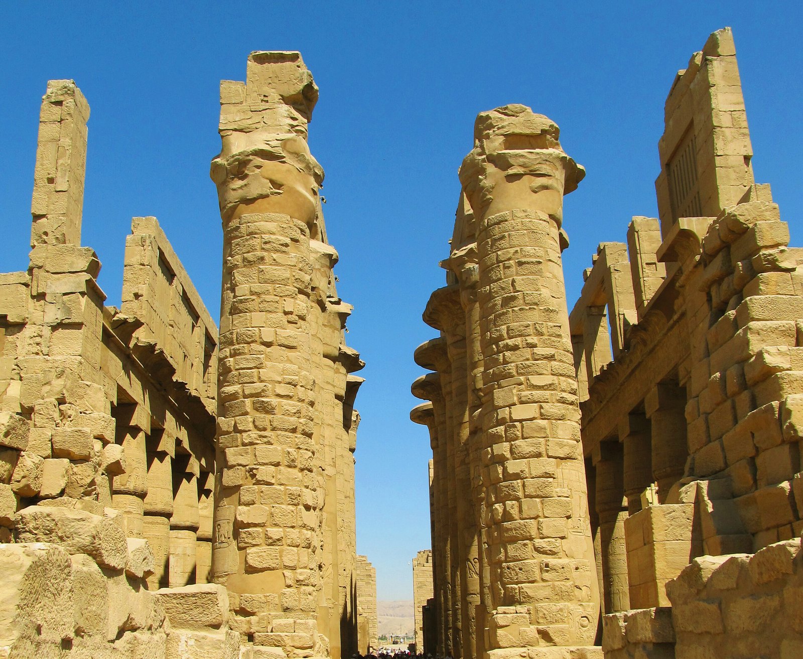 Due alte colonne della sala ipostila di Karnak tra i muri di pietra dorata, sotto un cielo blu intenso
