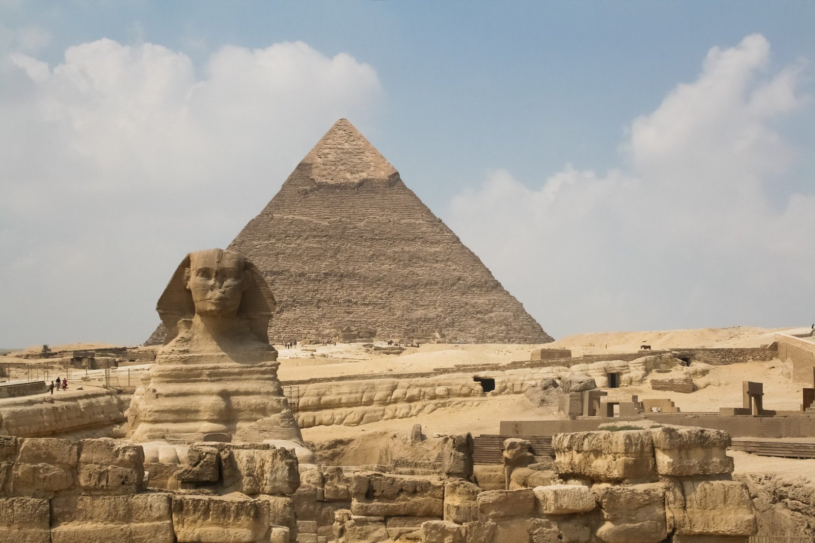 La Sfinge di Giza con una piramide alle spalle, sotto un cielo con grandi nuvole bianche