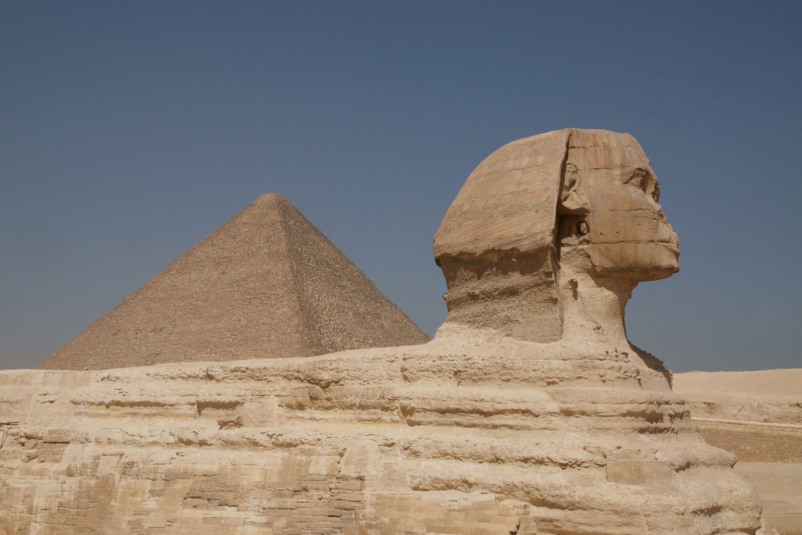 Il profilo della Sfinge di Giza con una piramide dietro, sullo sfondo del cielo blu
