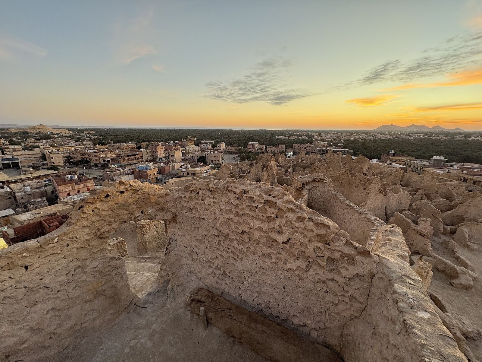 Il tetto della fortezza di Shali a Siwa al tramonto, con le case dell'oasi e le palme in lontananza