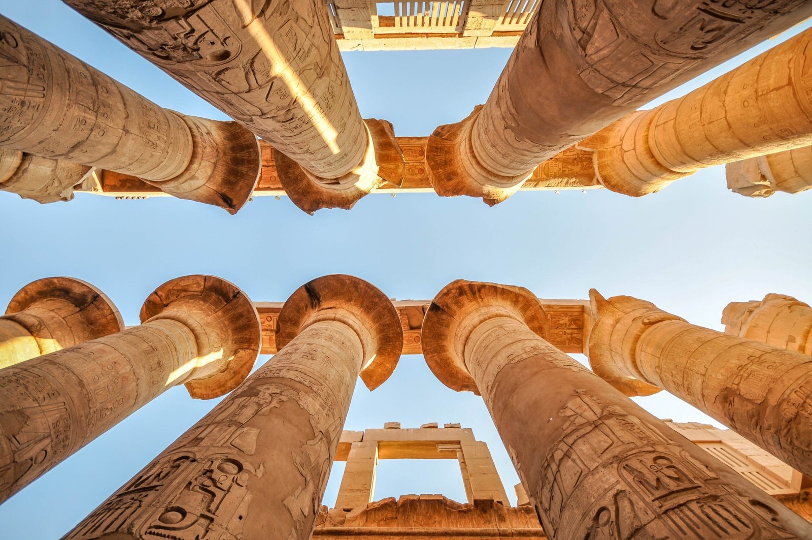 Colonne con capitelli aperti nella sala ipostila di Karnak viste dal basso, contro il cielo azzurro