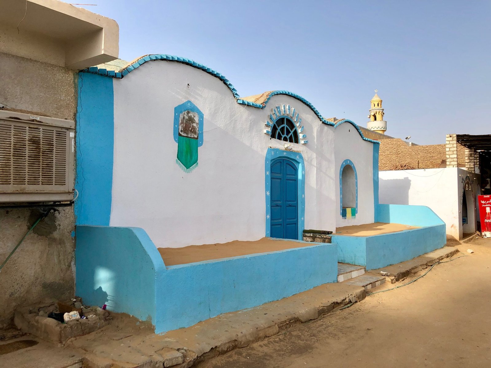 Una casa nubiana dipinta di bianco e azzurro, con la porta ad arco e il minareto sullo sfondo