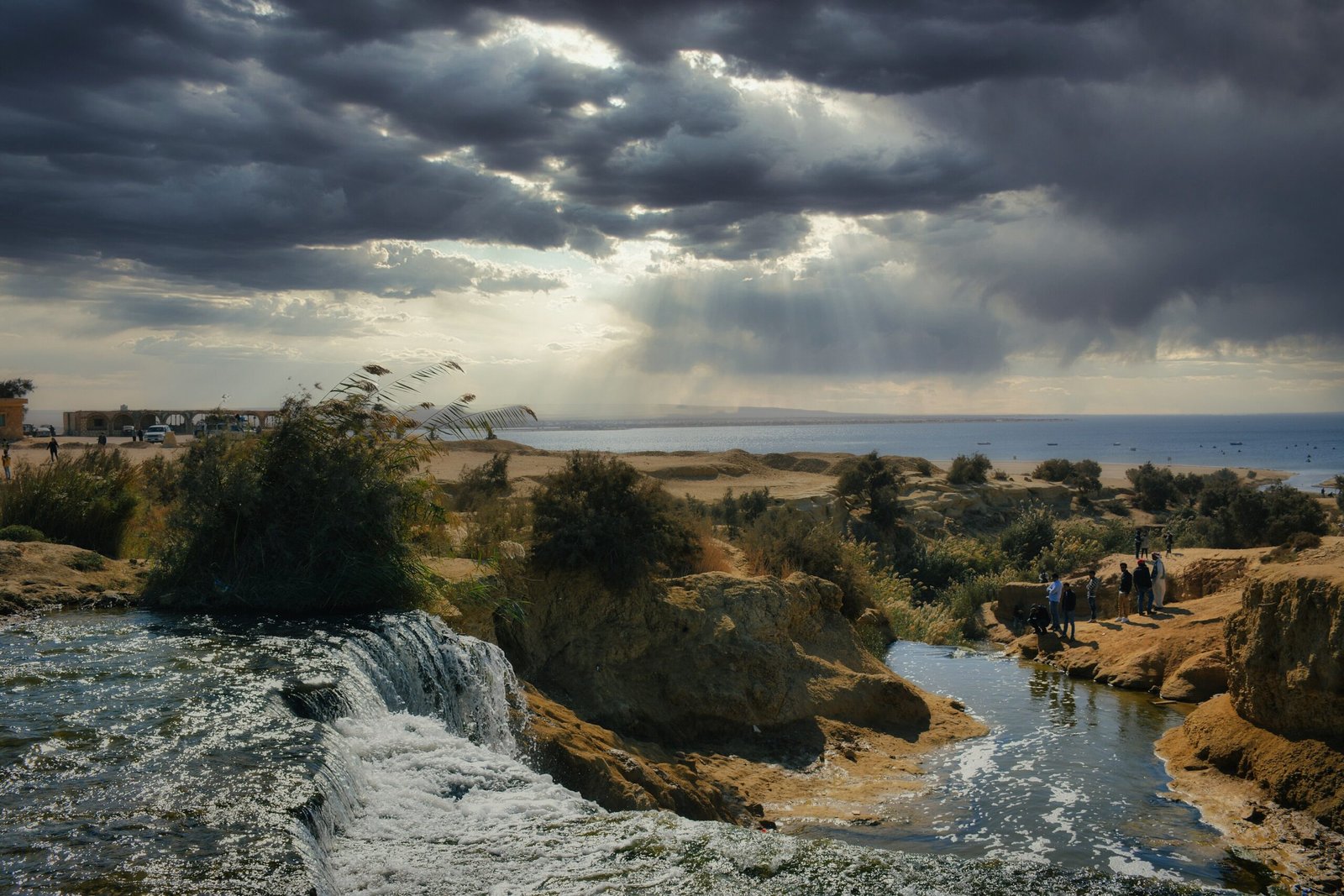 La cascata di Wadi el Rayan nel Fayyum tra le rocce, con il cielo carico di nuvole e raggi di sole sul lago
